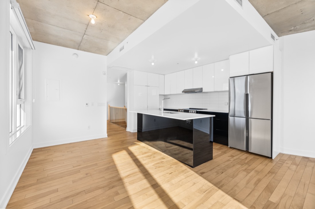 Cuisine de condo avec îlot noir laqué, armoires blanches et électroménagers en acier inoxydable