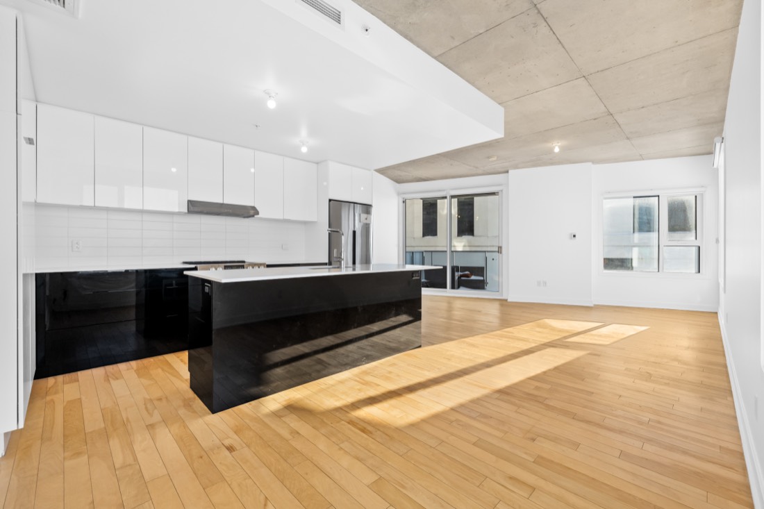 Aire ouverte d'un condo de style loft à Rosemont : cuisine à îlot noir, plafond de béton apparent et planchers d'érable