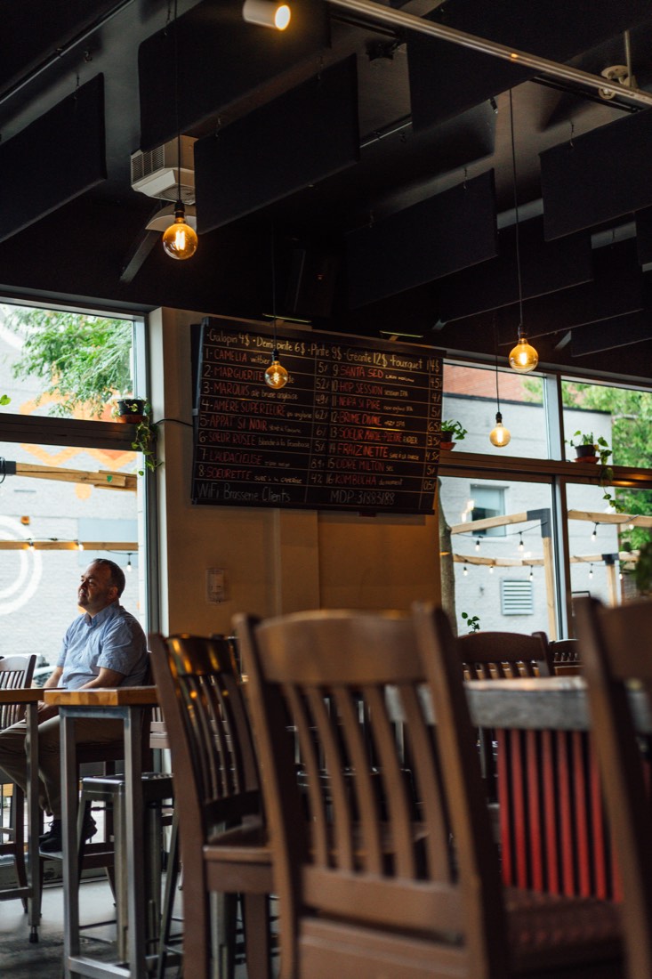 Salle de la brasserie Les Sœurs Grises : tables en bois et ardoise des bières sous des suspensions chaleureuses